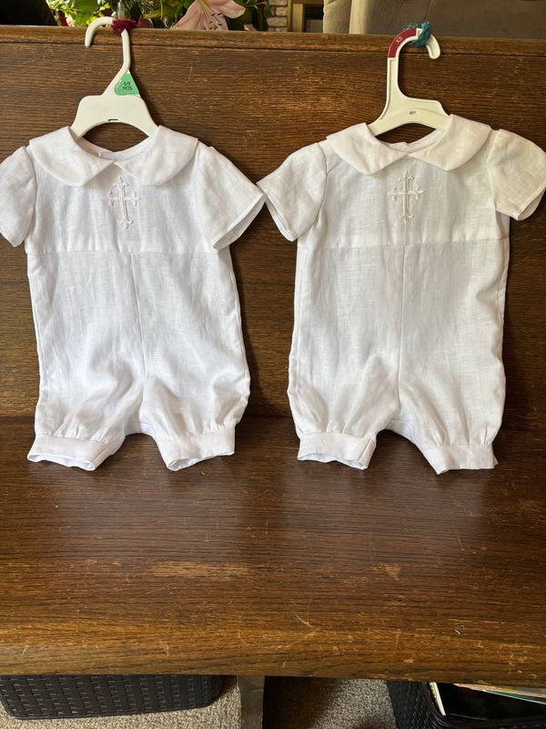 Two small white christening rompers with collars on hangers