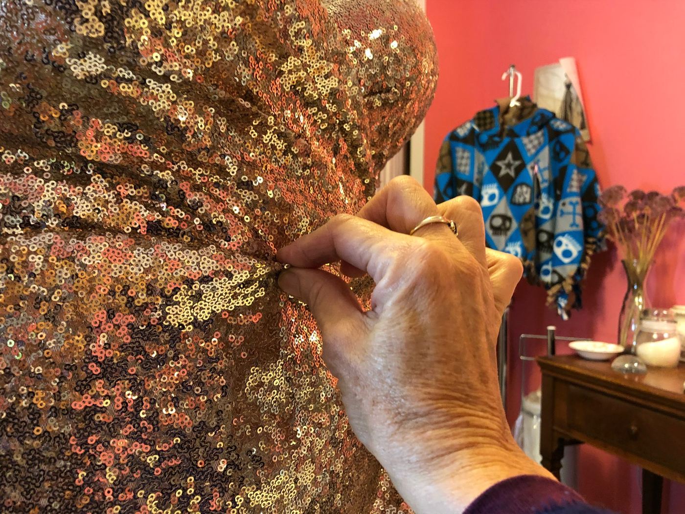 Wendy’s hand pinning the bodice of a gold sequin dress in her pink fitting room