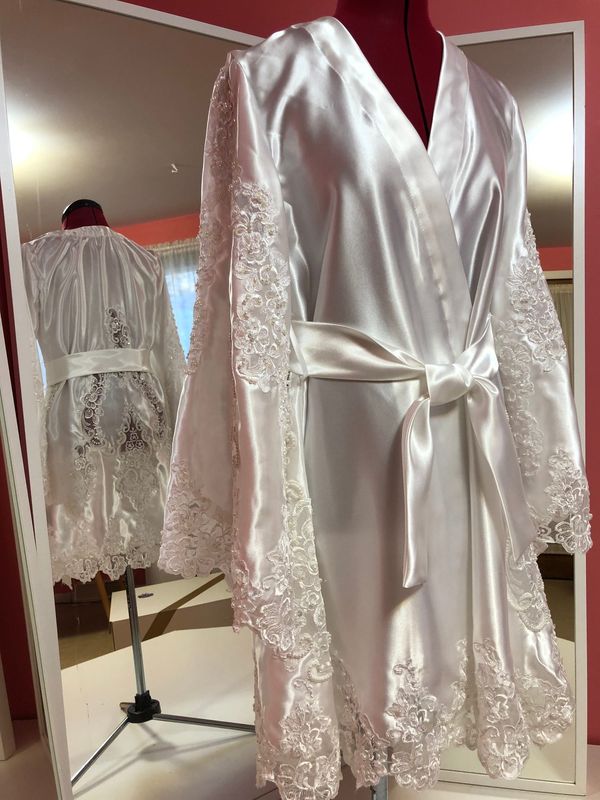 A satin robe with full lace sleeves and a bow sash on a dress form